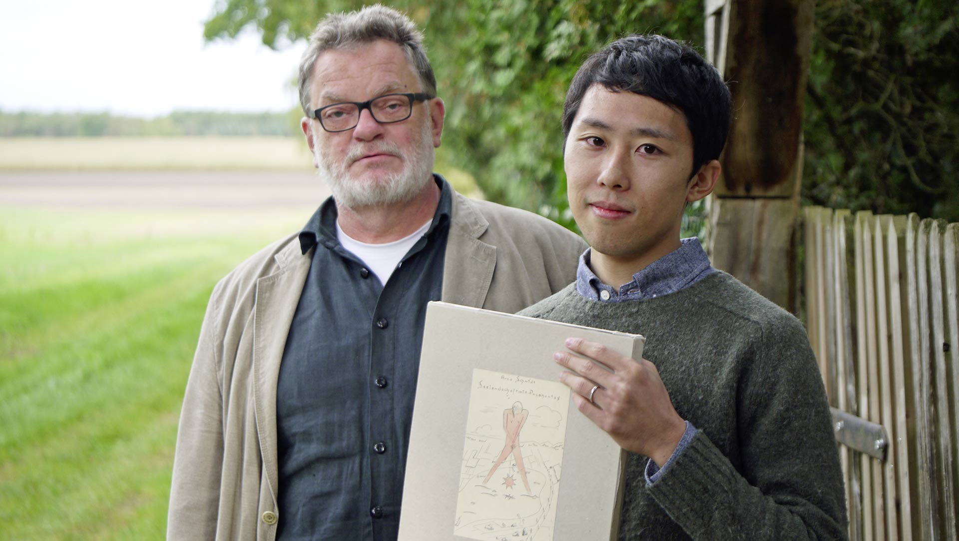 Jun Wada holding the original “Seelandschaft with Pocahontas” manuscript with Bernd Rauschenbach in front of Arno Schmidt’s former residence in Bargfeld.
