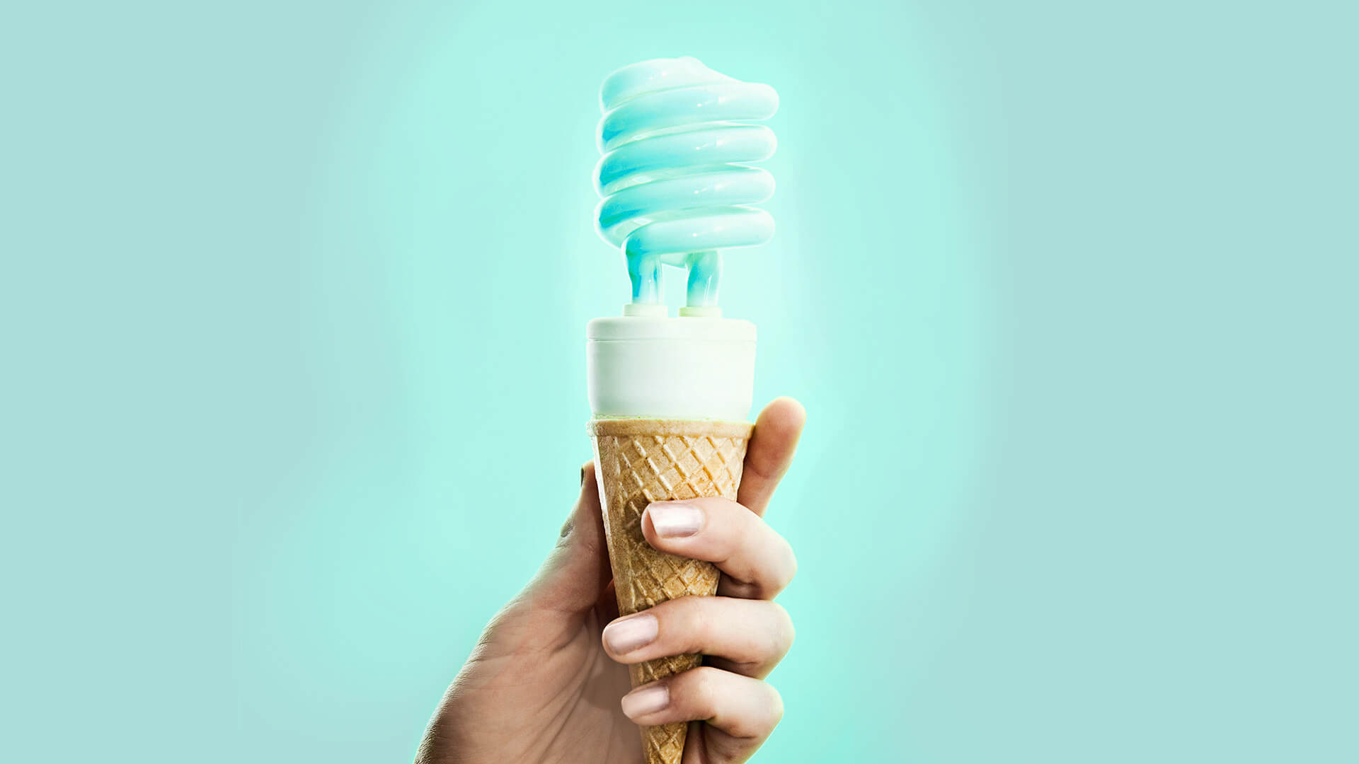    A hand holding an ice cream cone filled with a lightbulb